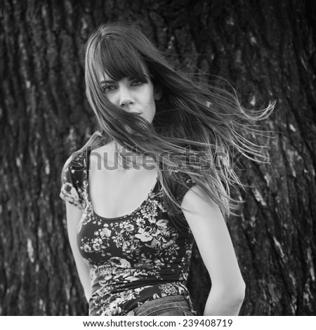 Black and white photo of woman posing near a tree with windy hair