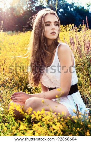 long-haired teen girl is sitting on flowers meadow