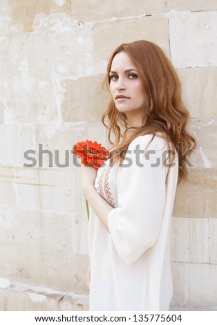 The beautiful girl with a long fair hair in a white blouse and with a flower in her hands