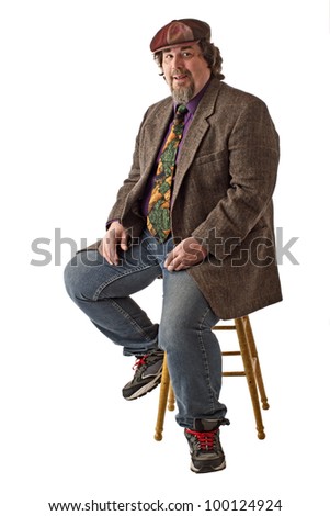 Man with large build sits on stool, dressed casually in tweed cap, jacket and jeans. He smiles and  sits forward with hands on knees. Vertical, isolated on white background, copy space.