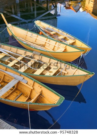 Group of traditional bright yellow painted wooden fishing dories roped together and moored at a dock in Lunenburg, Nova Scotia. Reflections of boathouses nearby. Vertical layout.