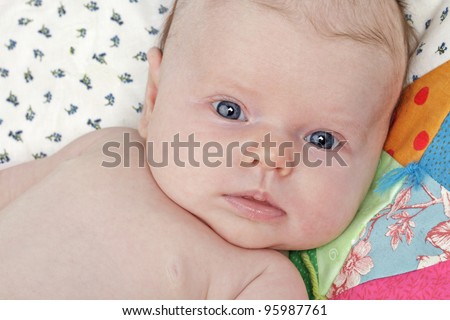 Closeup head and shoulders portrait of an alert, healthy, beautiful bright-eyed new baby. Colorful dainty patchwork quilt background, horizontal layout.