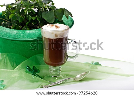 Glass of Irish coffee, green bowler hat with shamrocks, fabric and silver teaspoon in foreground, isolated white background. Horizontal layout and copy space.
