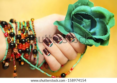 Ethnic motifs on the nails female young hands with beaded bracelet with turquoise rose on a yellow background.