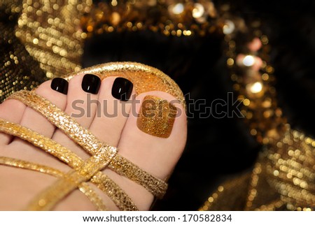 Luxury pedicure with black and gold lacquer on women\'s toes on the black and brilliant background.