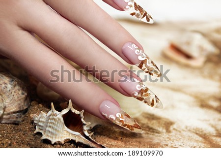Nail design with brown and white these little shells inside gel nails on the background of shells and sand.