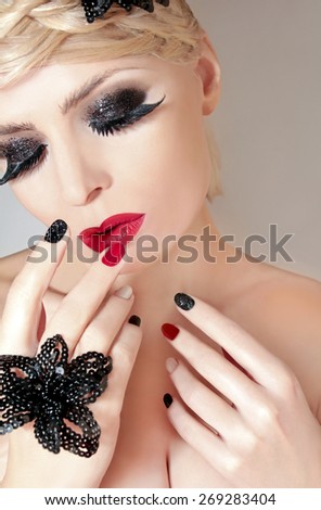 Makeup with red lips,black eyelashes,bushy eyebrows and a multicoloured manicure on a woman with blond hair.