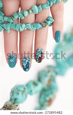 Manicure with beads and turquoise in the form of small stones and jewelry made of turquoise on the woman\'s hand.