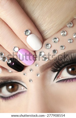 The nails on the short form with rhinestones and colored lacquers on the girl with blond hair and black false eyelashes.