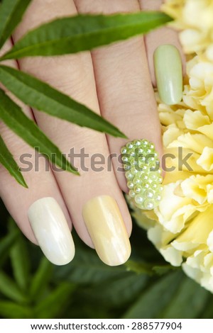 Nail design with pearl rhinestone and multi-colored mother of pearl lacquer on a woman\'s hand.