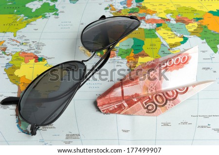 Sunglasses and origami plane made from money on the world map
