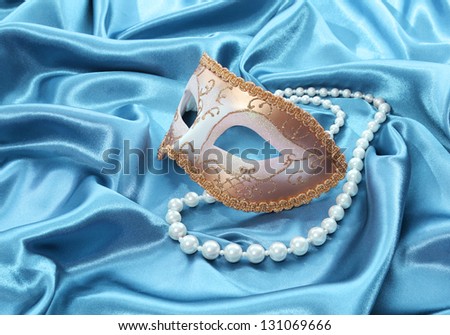 glitter gold mask and pearl necklace on turquoise silk drape background