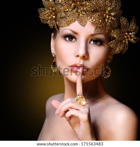 Fashion Girl with Gold Jewelries over black background. Beauty young woman with finger on her sexy lips showing Hush. Decorated Hairstyle. Luxury Portrait