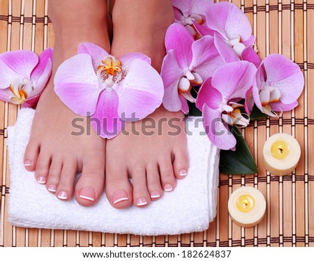 Pedicure. Beautiful female feet with french manicure and pink orchid flowers on bamboo mat.  Foot care. Spa Salon