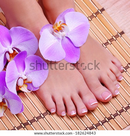 Pedicure with pink orchid flowers on bamboo mat. Beautiful female feet with french manicure. Foot care. Spa