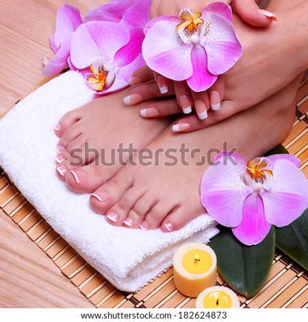 French Manicure on Beautiful Female Feet and Hands with pink orchid flowers on bamboo mat. Nail care. Pedicure. Spa Salon