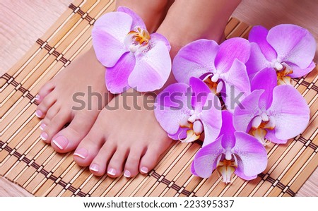 Pedicure. Female feet with pink orchid flowers on bamboo mat. Foot care. Spa