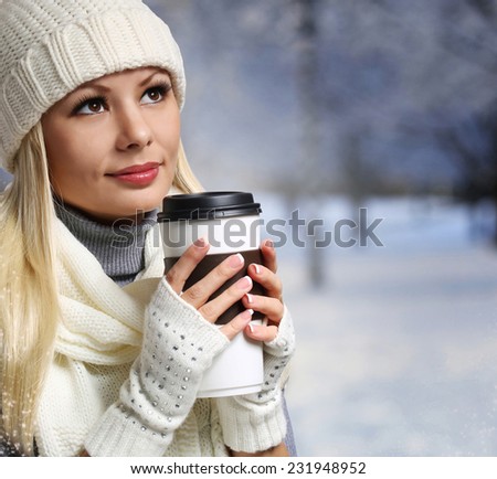 Girl with Coffee Cup over Winter background. Blonde Beautiful Young Woman in Knitted Hat and Scarf. Portrait
