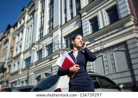 businesswoman with documents and tablet in hand, talking on the phone on the background of vintage buildings