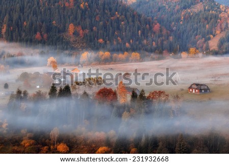 Autumn Ukrainian Carpathian village in the mist.\
Autumn hillsides surrounding mountain village, on the slopes of spreading fog.