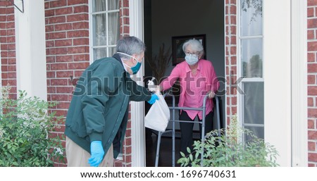 An elderly woman with a walker who is at high risk because of the coronavirus COVID19 gets meals or groceries delivered to her house by a volunteer working with a benevolent organization.
