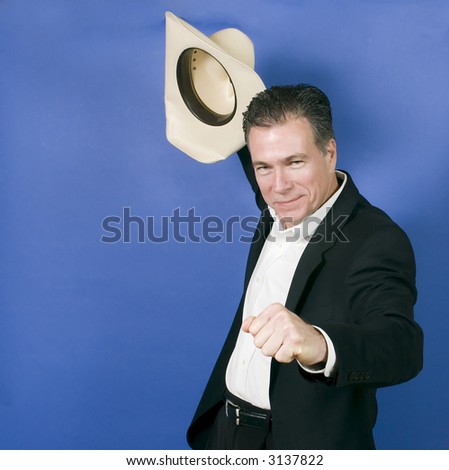Mature, handsome, white male wearing a black suite and a white shirt holding a cowboy hat with one hand as if in celebration or exhilaration.