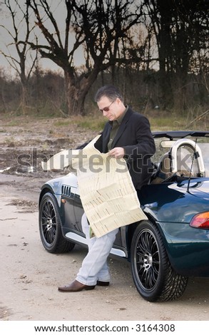 Man who has pulled off the road into an isolated area reading a map trying to figure out where he is.