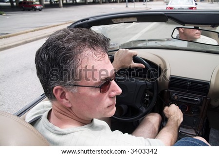 Man in a convertible driving with the top down.