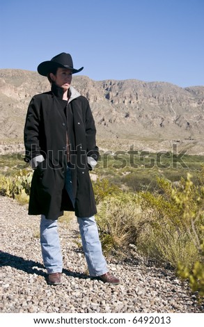A woman dressed in western attire, surveying the harsh environment surrounding her.