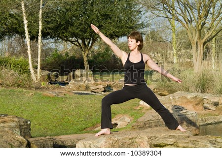A woman standing on a rock in a yoga posture called warrior pose.