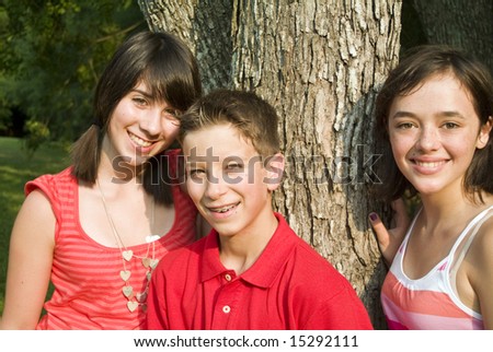 Three happy adolescents standing by a tree in the afternoon sun.