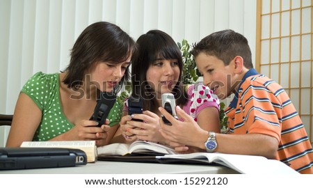Three school kids playing around with their cell phones instead of studying.