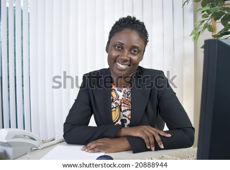 A lovely young Black woman in an office environment smiling a kind, friendly smile.