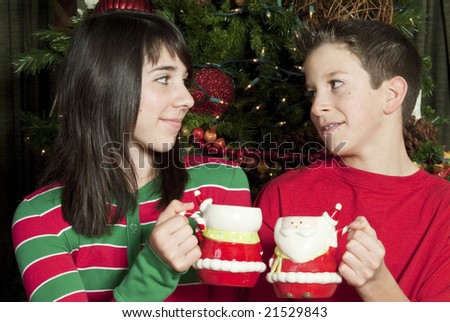 Two children sitting by of a lovely Christmas tree enjoying mugs of hot chocolate.