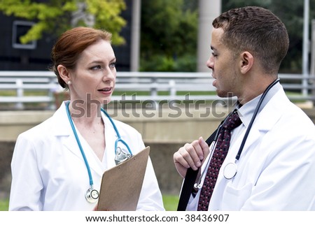 Two doctors on break in a city green space, engaged in friendly conversation.