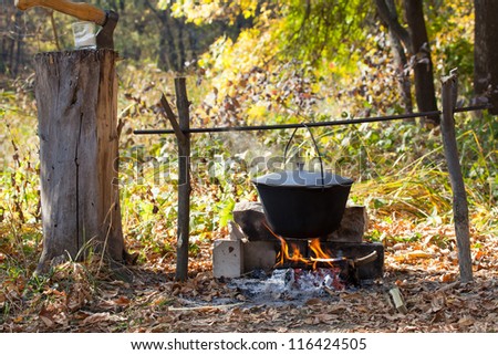 Outdoor summer. Cooks porridge in a pot on the fire