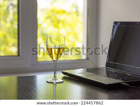 Glass of white wine and laptop in front of the window