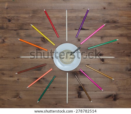 cup of coffee in the center and colored pencils around on old wooden table