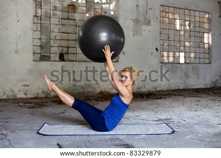 Fitness exercise / Beautiful blond woman exercises with a fitness ball in an abandoned house