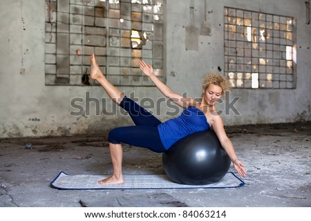 Beautiful blond woman exercises with a fitness ball in an abandoned house