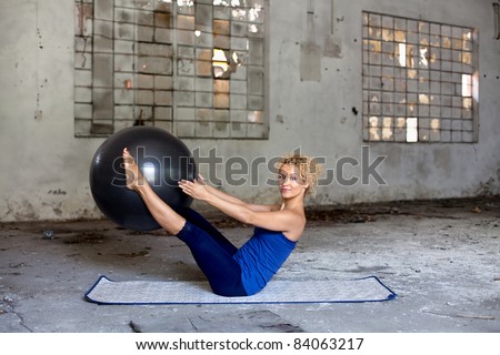Beautiful blond woman exercises with a fitness ball in an abandoned house