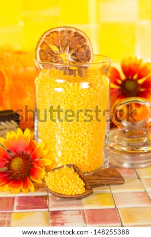 Orange citrus bath salts with natural healthy plant extracts displayed in a wooden scoop and clear glass jar on a tiled bathroom surface