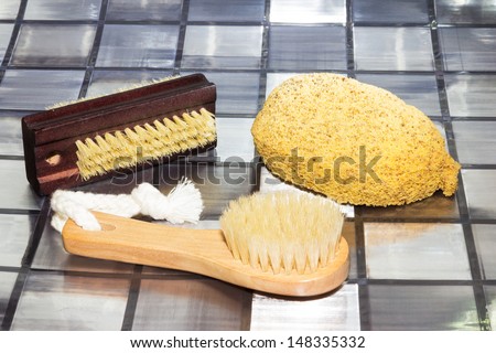 Bathing accessories lying on a tiled surface in a bathroom with a nail brush, wooden body brush and sponge