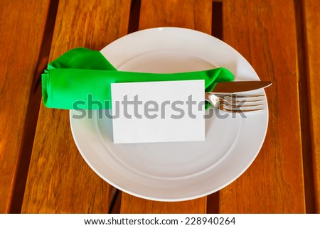 Dishware and blank paper card on table in restaurant - food background