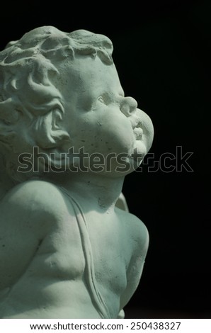 Air-kissing angel, stone cherub, sculpture in a graveyard, isolated on black