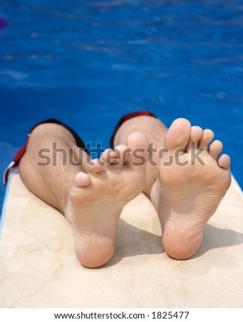 Bottoms of feet resting on a diving board with pool water in background for copy space