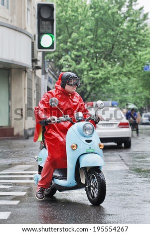 SHANGHAI-MAY 4, 2014. Chinese man in red rain-wear on a retro scooter. Shanghai has a humid subtropical climate, its summer is very warm and humid, with occasional downpours or freak thunderstorms.