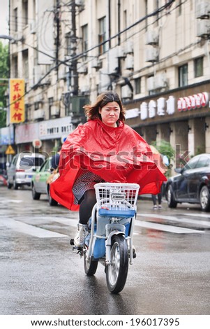 SHANGHAI-MAY 4, 2014. Chinese girl in red rain-wear on an e-bike. Shanghai has a humid subtropical climate, its summer is very warm and humid, with occasional downpours or freak thunderstorms.