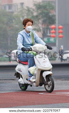 BEIJING-OCT. 11 ,2014. Woman on an e-bike in smog blanketed city. A concentration of PM2.5, small particles that poses a huge health risk, hit 462 according U.S. Embassy pollution monitor in Beijing.