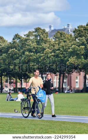 AMSTERDAM-AUG. 24, 2014. Caucasian couple walks on a sunlit Museum Square. A popular tourist square where the famous Rijksmuseum, Van Gogh Museum, Stedelijk Museum and Diamond Museum are located.